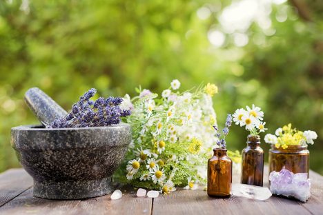 Homeopathy and herbal medicine concept. Granite mortar and pestle with flowers and herbs, glass bottles with flowers and nature crystals stones